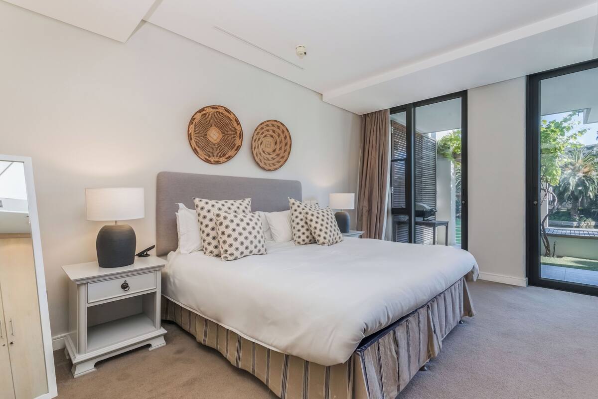 Une chambre à coucher avec un grand lit, deux tables de chevet, une commode, une fenêtre avec vue et deux éléments décoratifs fixés au mur.