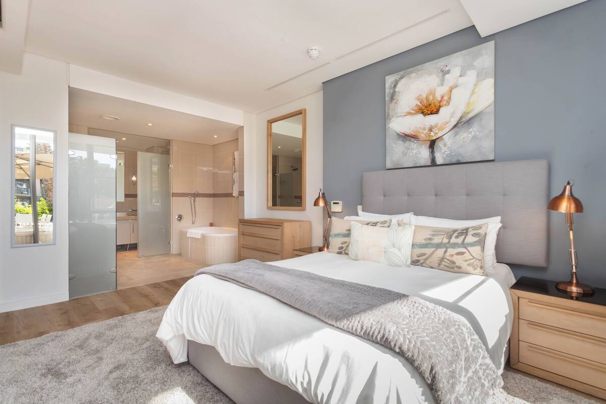 Une chambre à coucher moderne avec un grand lit, des lampes de chevet, un miroir et un tableau accroché au mur.