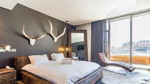 A modern hotel room with a large bed, a leather armchair, and a city view. - Mountain Marina Luxury Apartments (Cape Town)