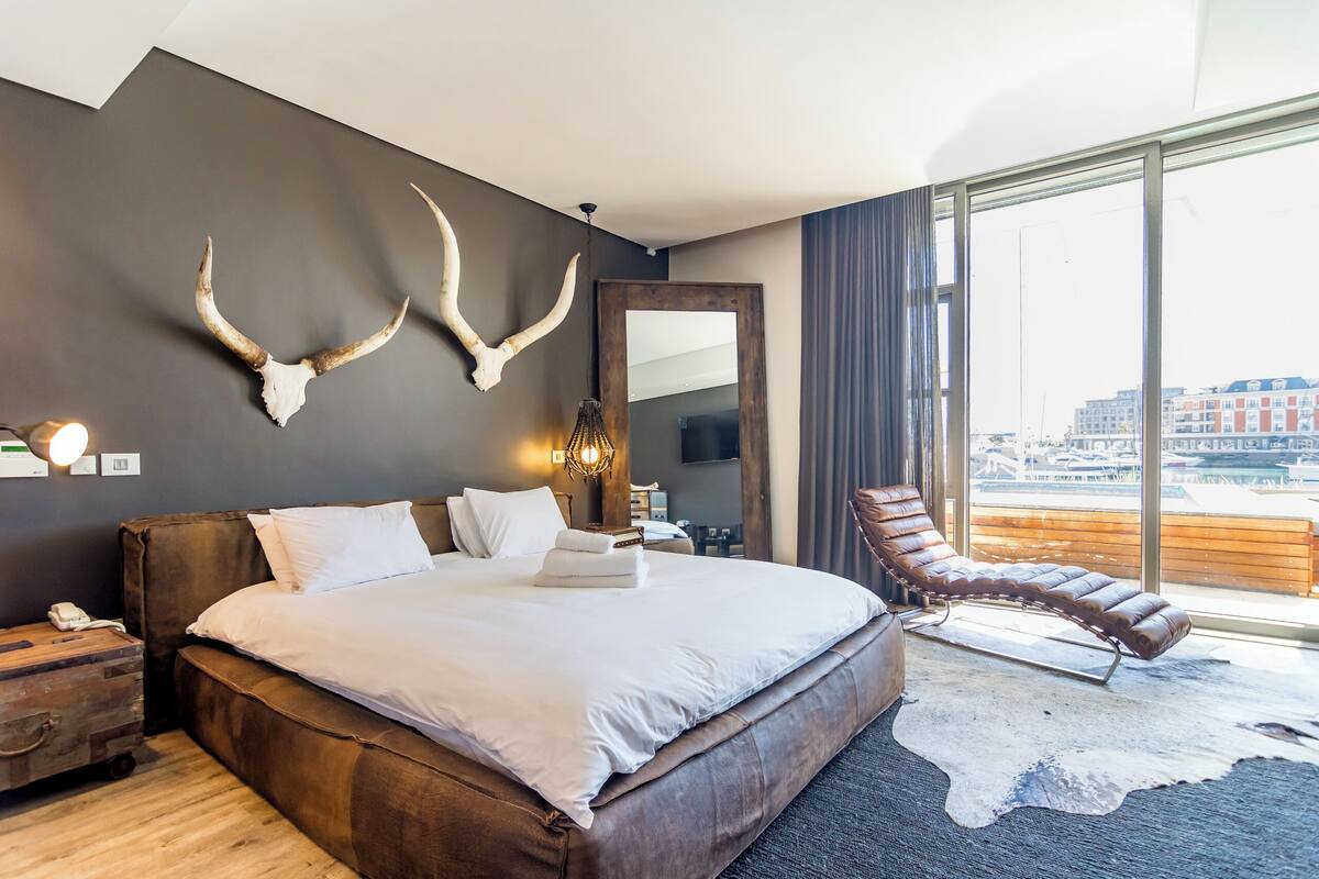 Une chambre d’hôtel moderne avec un grand lit, un fauteuil en cuir et une vue sur la ville.