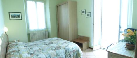 Un dormitorio con cama, escritorio, silla, radiador y ventana.