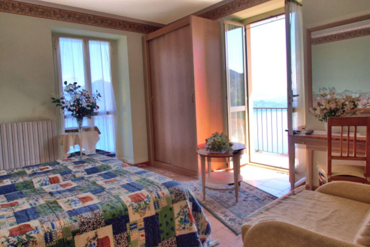 Une chambre avec un grand lit, une petite table sur laquelle est posée une plante, une chaise et une vue sur l’extérieur grâce à une porte coulissante.
