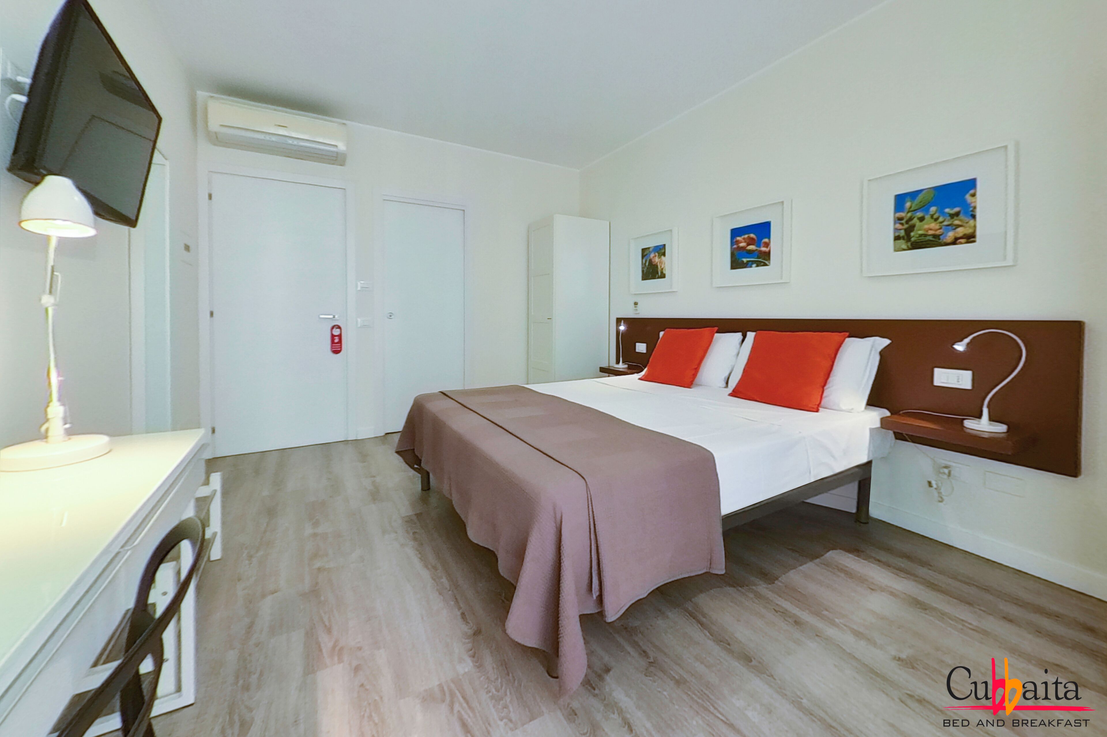 A hotel room with a bed, a desk, a chair, a TV, and a wardrobe.