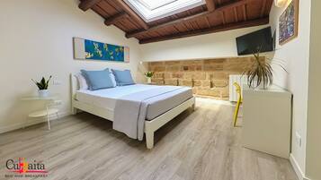 A bedroom with a bed, a skylight, a stone wall, a TV, and a plant.