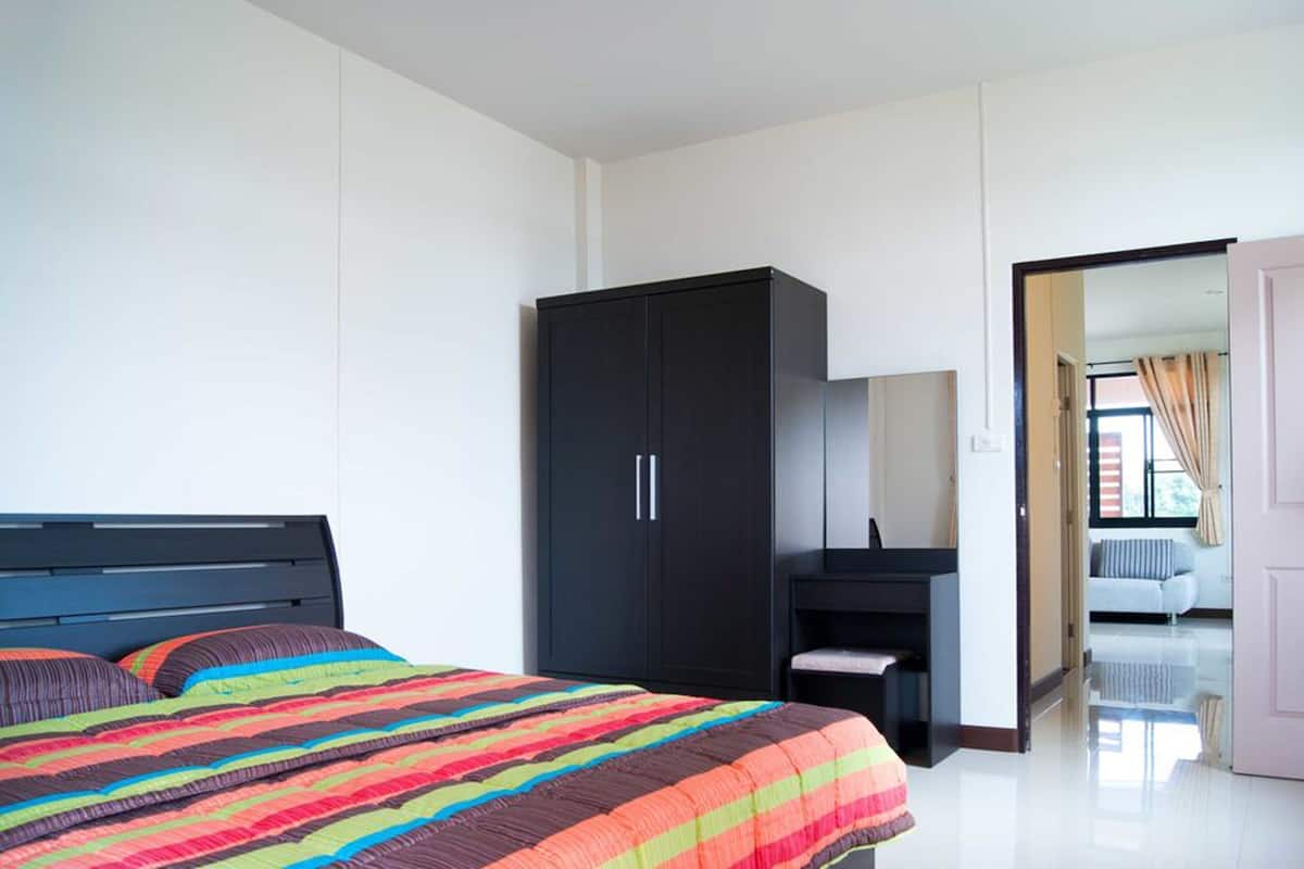 Ein Schlafzimmer mit Bett, Schrank, Schreibtisch und Blick auf einen anderen Raum.