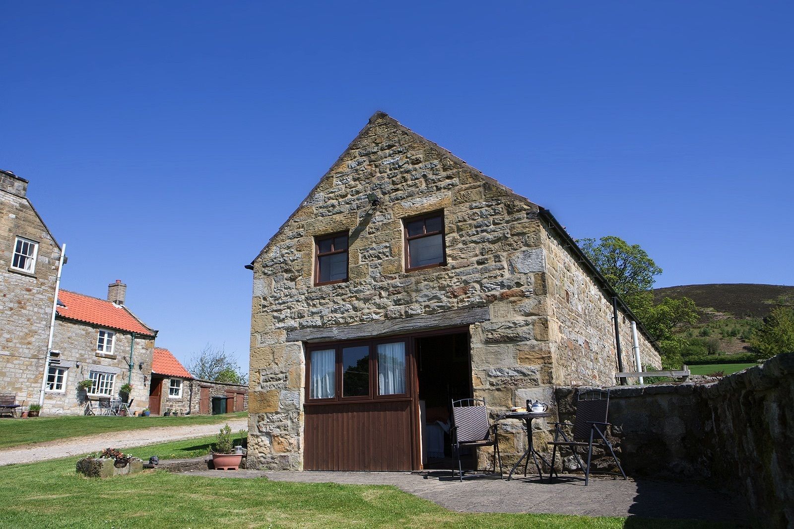 A stone building with a gabled roof, a wooden door, and a small porch area with outdoor seating.