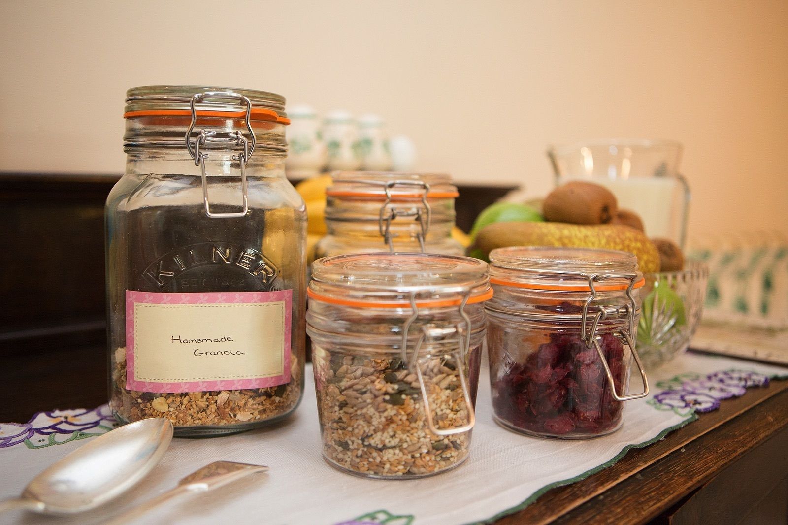 Un plan de travail de cuisine avec divers bocaux en verre contenant du granola et des fruits secs, une cuillère et un bol de fruits.