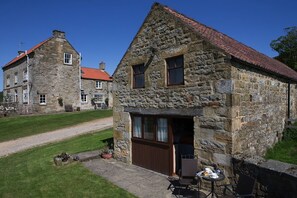 A stone cottage with a red-tiled roof, a wooden door, and a small patio with a table and chairs. - Easterside Farm bed & Breakfast (York)