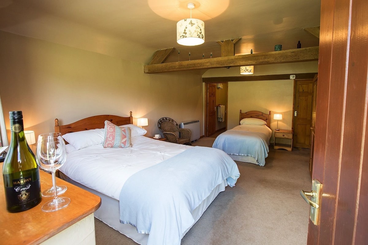 A hotel room with two beds, a wooden ceiling, a small table with a bottle of wine, and a chair.
