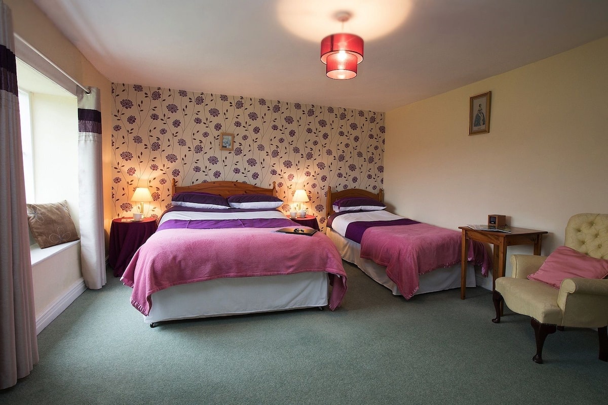 A bedroom with two beds, a chair, a table, and a small bedside table with a lamp.