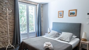 Un dormitorio ordenado con una cama grande, una mesita de noche, una lámpara de pie y vistas a través de una ventana.