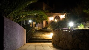 Una escalera nocturna que lleva a un edificio de paredes de piedra, con una palmera a la izquierda.