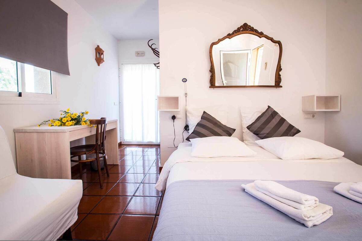 Une chambre d’hôtel avec un lit, un bureau, une chaise, un miroir et une fenêtre.
