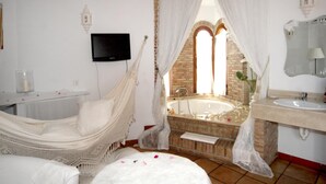 Un baño con bañera, lavamanos, televisor y una silla de mimbre.