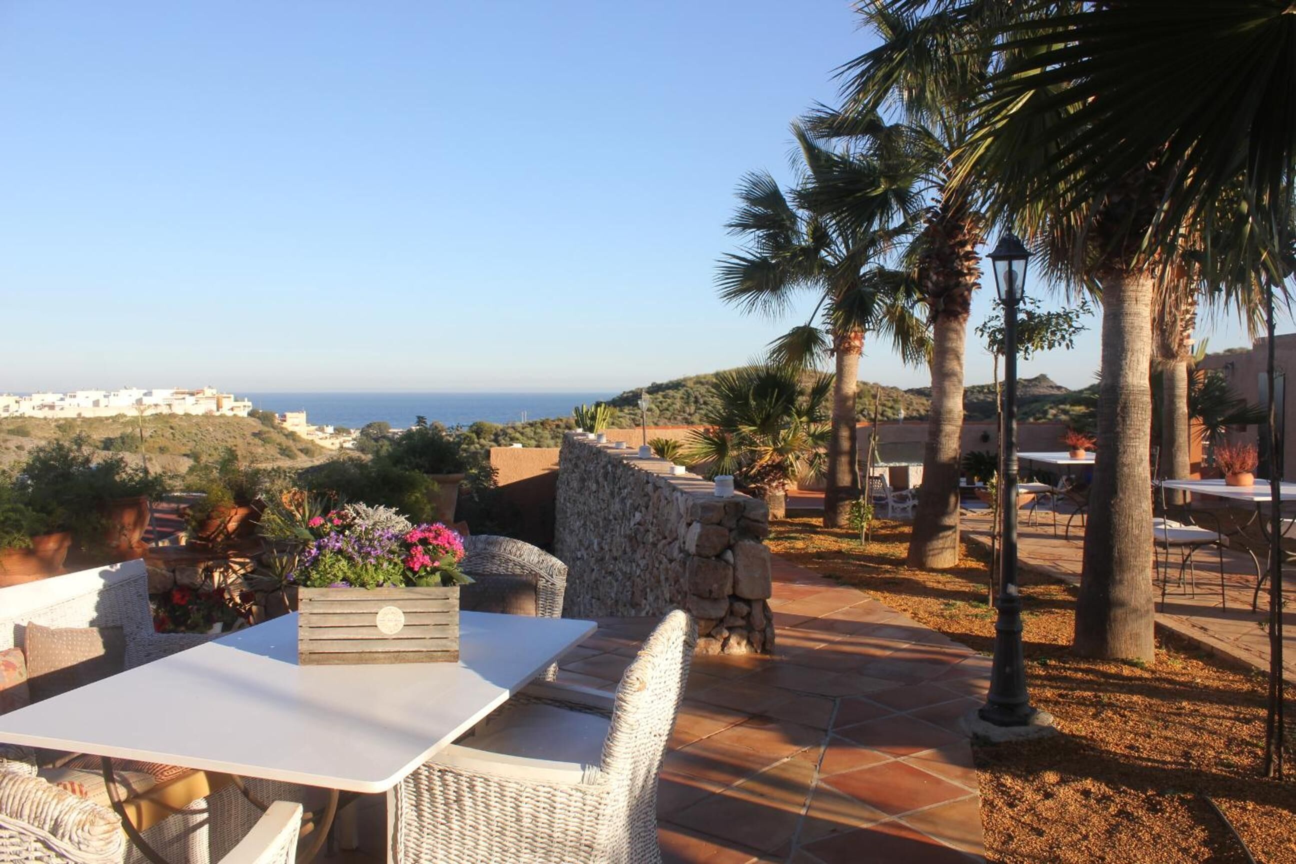 An outdoor patio with wicker furniture, a stone wall, and a view of the sea.