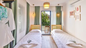 A twin room with two beds, a wooden headboard, a hanging light fixture, and a view of greenery outside. - Bahar Pansiyon (Kas)