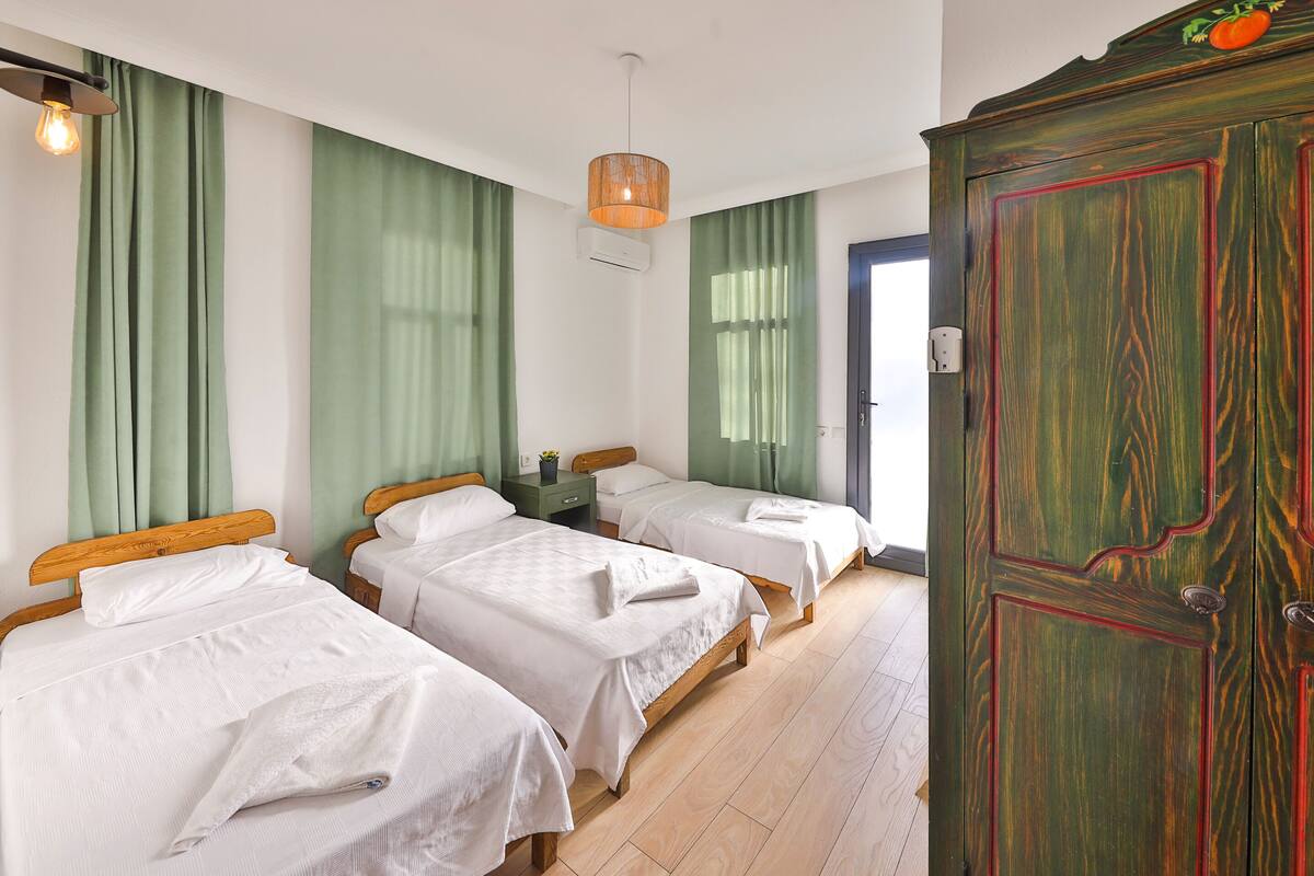 A room with three beds, a wooden wardrobe, and a hanging light fixture.