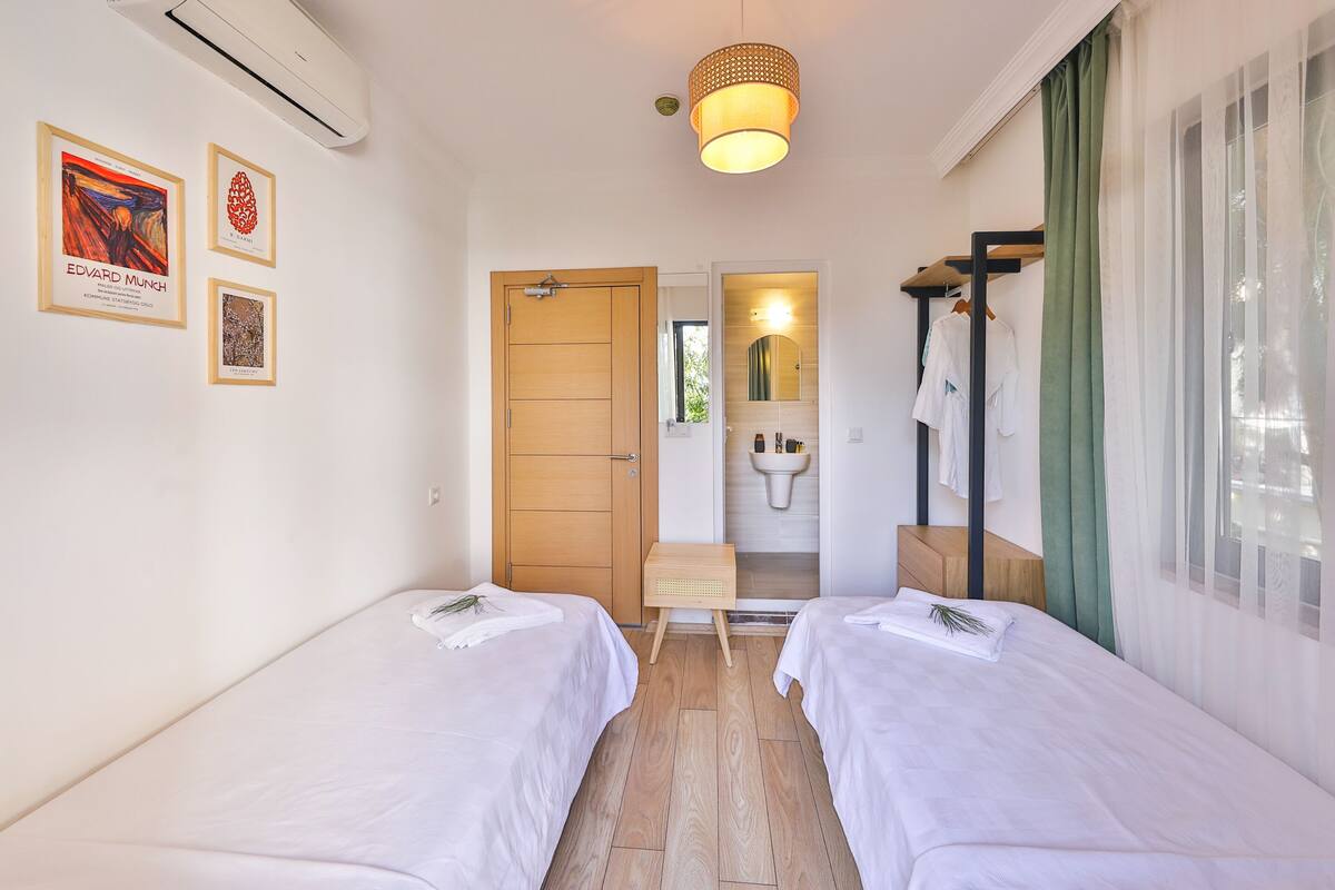 A hotel room with two beds, a wooden door, a small table, a mirror, and artwork on the wall.