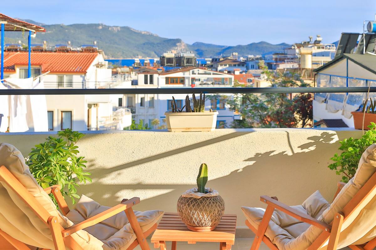A balcony with two beige lounge chairs, a small table, and a potted cactus.