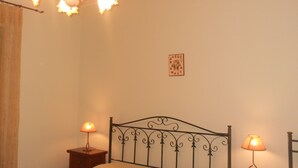 Een slaapkamer met een bed, twee nachtkastjes, een kroonluchter en een aan de muur hangend schilderij.