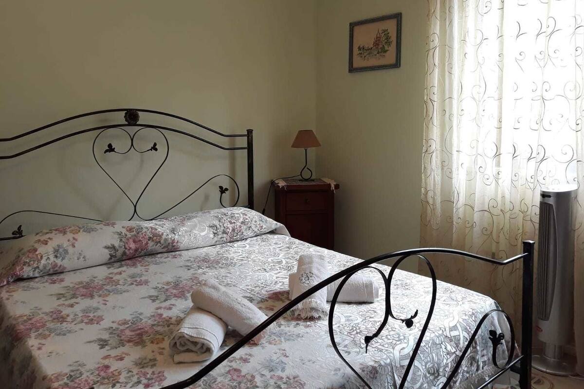 Un lit bien fait, avec une tête de lit en forme de cœur, une petite table de chevet avec une lampe et un tableau encadré accroché au mur.