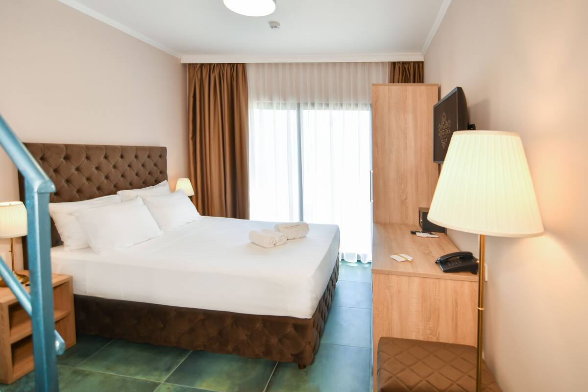 A hotel room with a large bed, a desk with a lamp, a telephone, and a television.