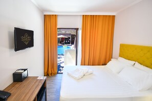 Une chambre d’hôtel équipée d’un lit, d’un bureau, d’une télévision et offrant une vue sur l’espace extérieur avec piscine.