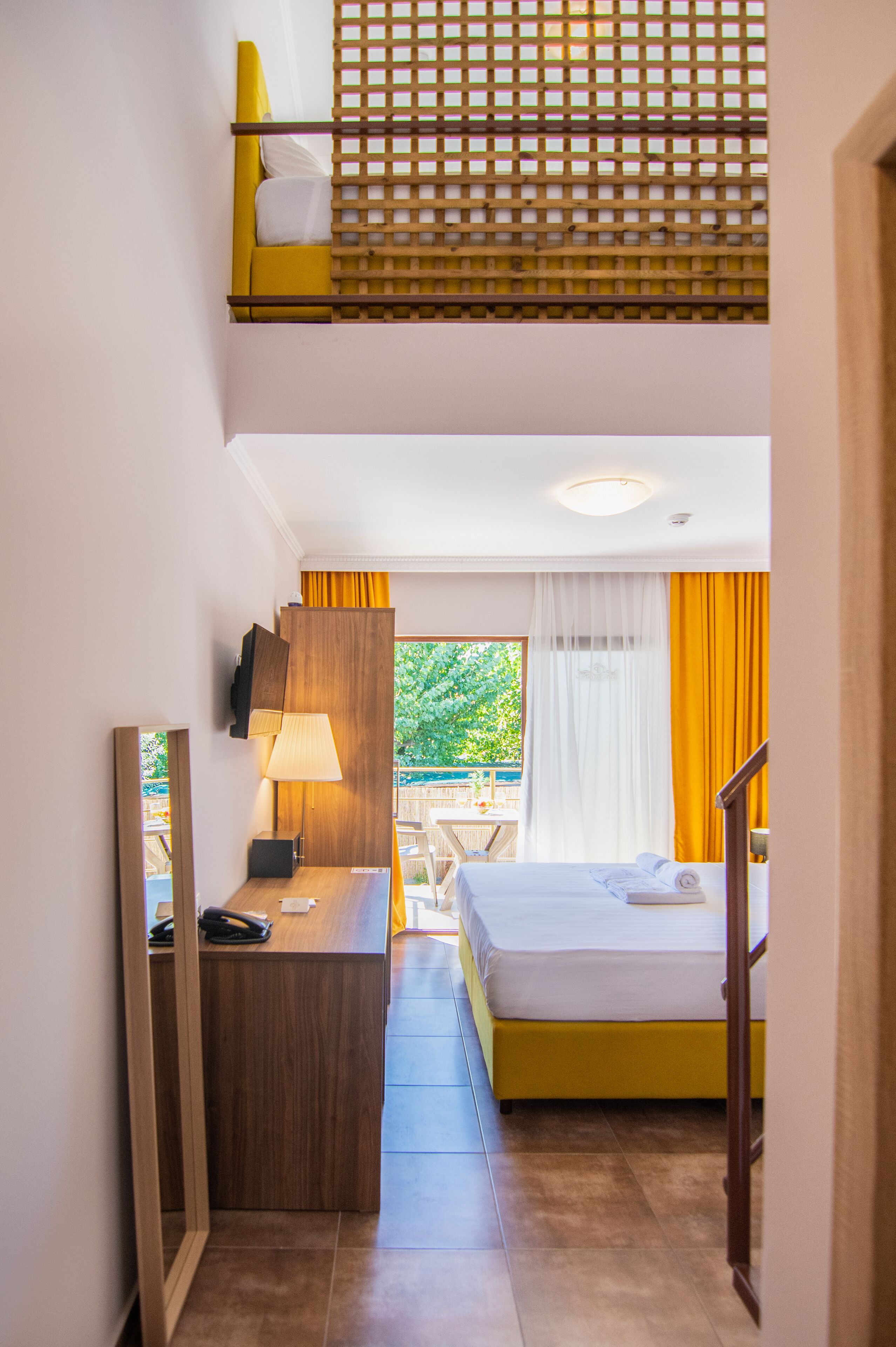 Ein Hotelzimmer mit Etagenbett, einem Schreibtisch mit Lampe, einem Spiegel und Blick ins Freie durch ein Fenster.
