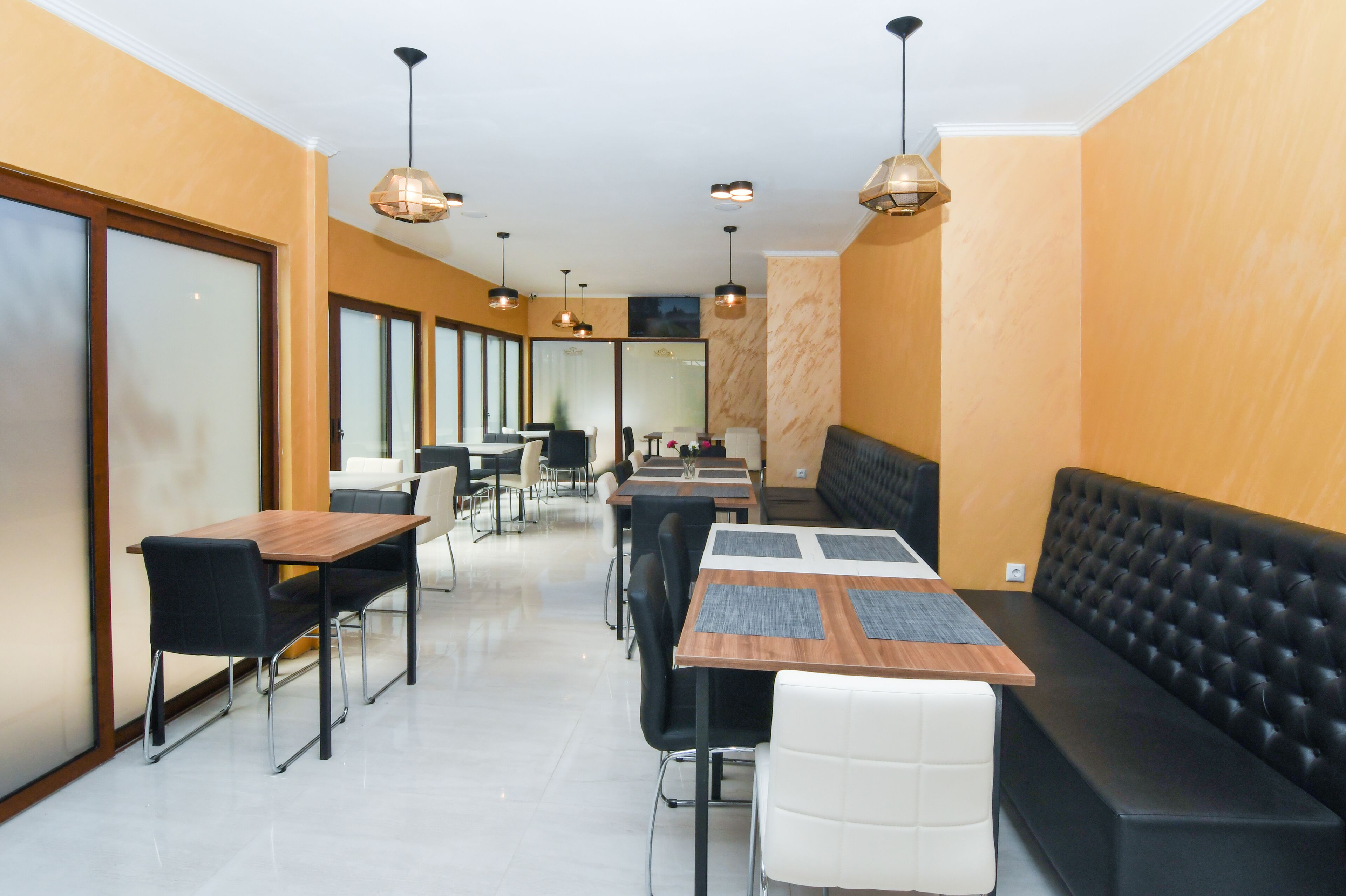 A modern dining area with tables and chairs, a black cushioned bench, and pendant lighting.