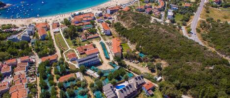 An aerial view of a coastal resort with beach access, multiple buildings, and a swimming pool area.