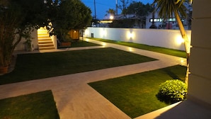 Un espacio exterior bien iluminado con un camino pavimentado, césped verde y una pared blanca.