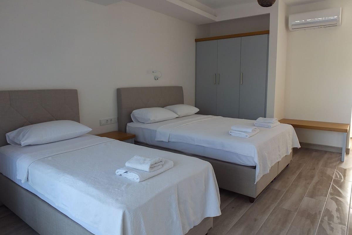 A hotel room with two beds, a wardrobe, an air conditioning unit, and a wooden floor.