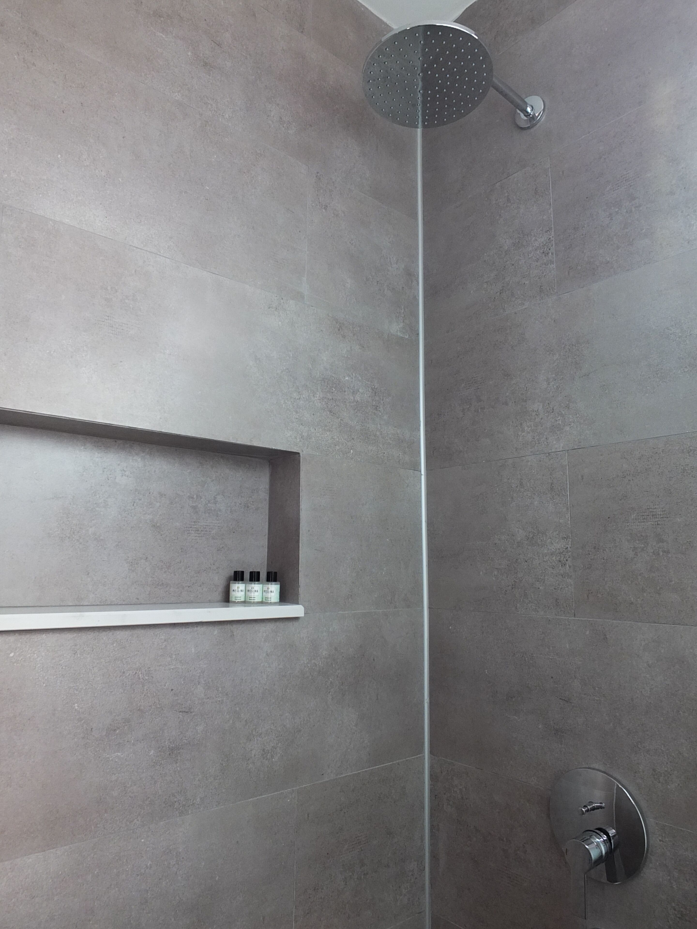Una doccia moderna con soffione a pioggia, uno scaffale con articoli da toilette e un rubinetto a parete.
