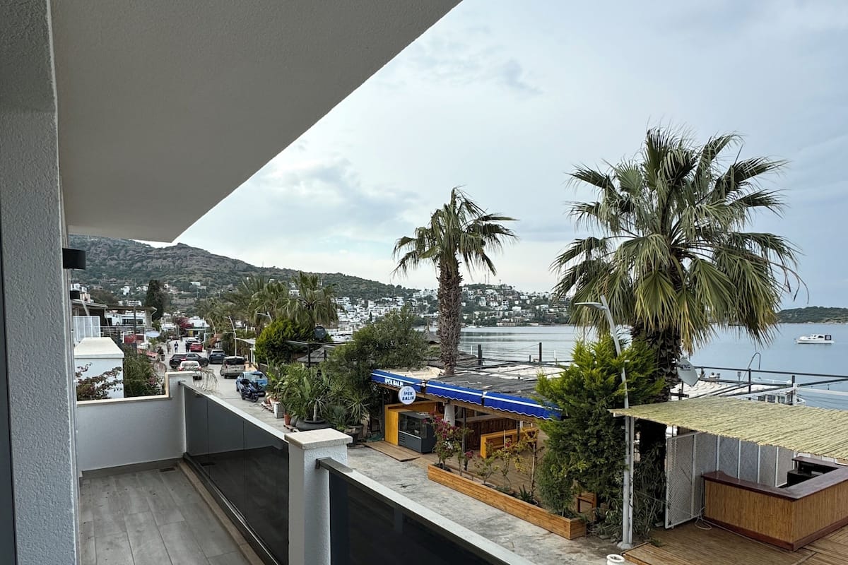 A balcony with a view of a beach, palm trees, and a town in the background.