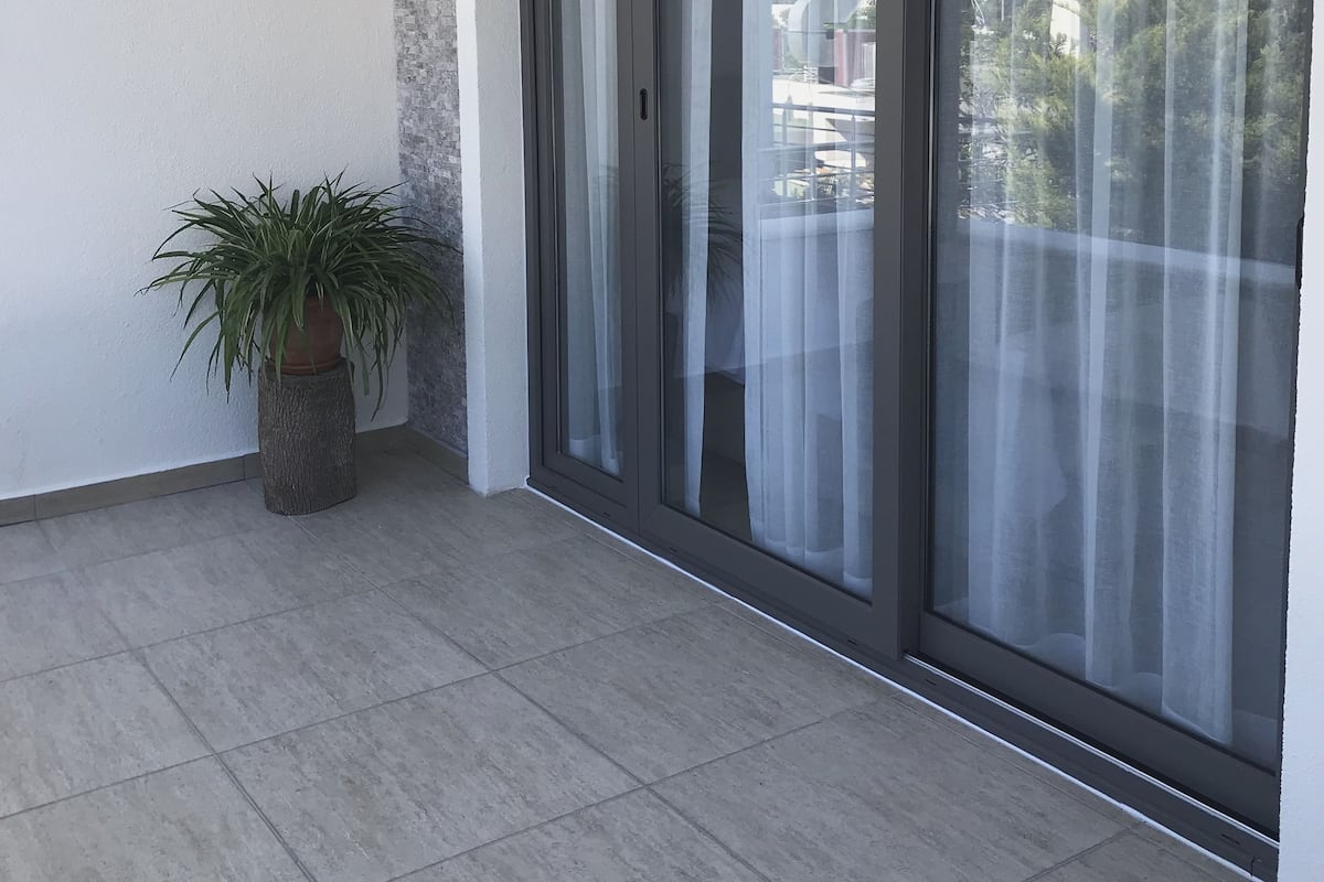 A balcony with a potted plant, a sliding glass door, and a tiled floor.