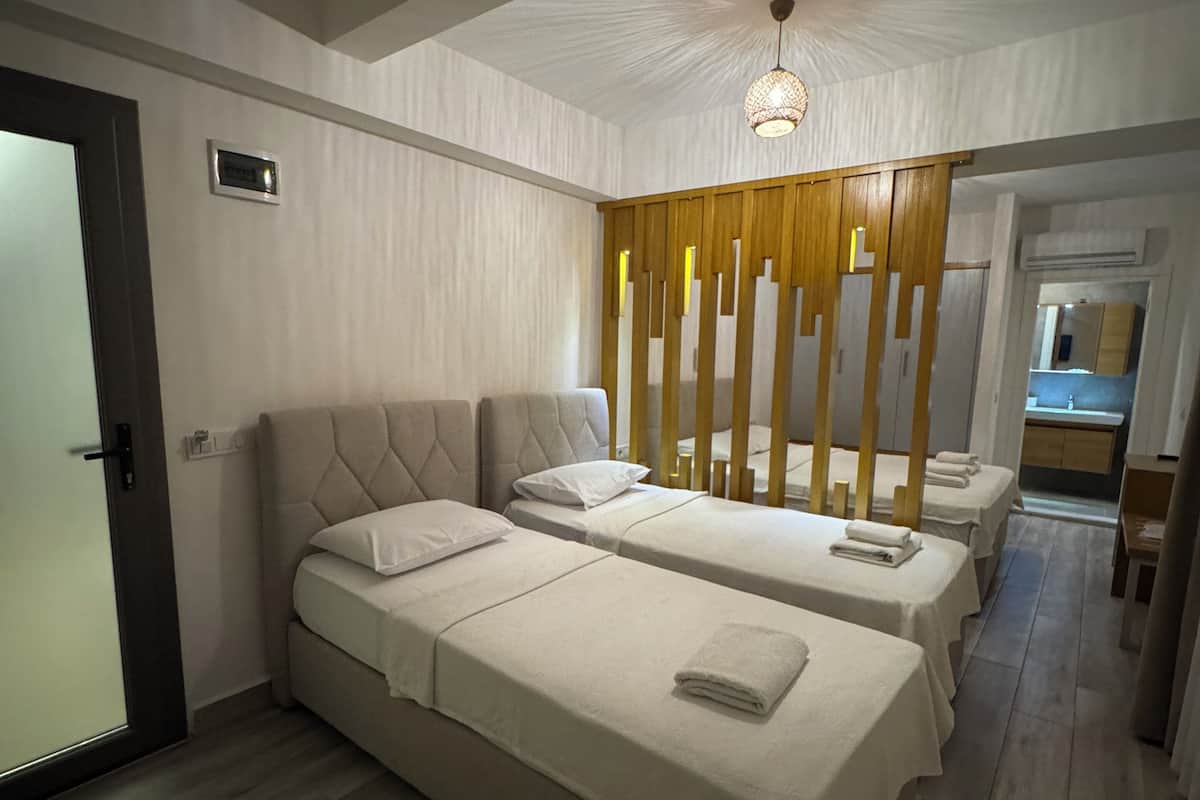 A hotel room with two beds, a wooden partition, a ceiling light, and a visible bathroom.