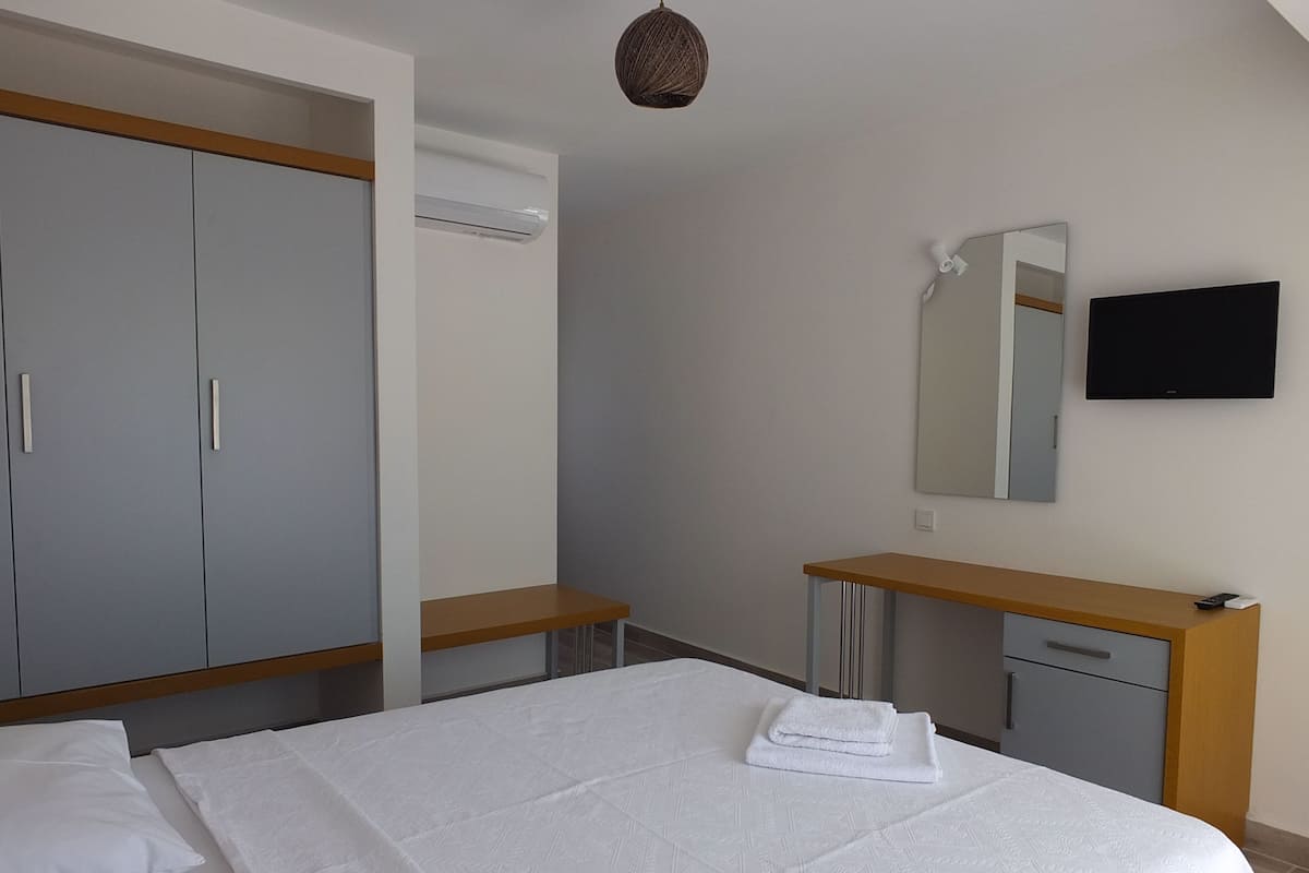 A bedroom with a bed, a wardrobe, a vanity with a mirror, and a television on the wall.