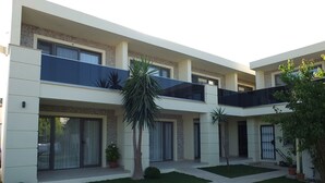 Un edificio moderno de varios pisos con techo plano, ventanas amplias y un patio central con césped y plantas en macetas.