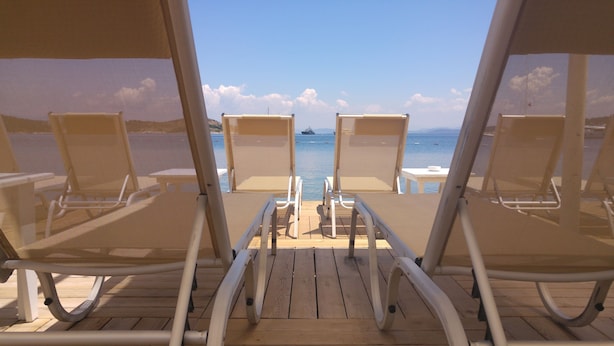Una terraza con dos sillones de descanso frente a un mar tranquilo y un barco a lo lejos.