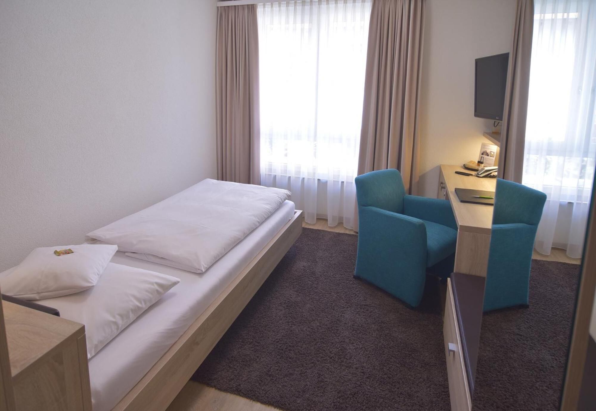 A hotel room with a single bed, two chairs, a desk, and a TV.