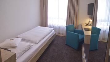 A hotel room with a single bed, two chairs, a desk, and a TV.