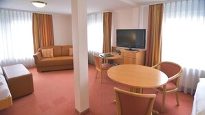 Quarto de hotel com sofá, mesa redonda e cadeiras, televisão e cama.