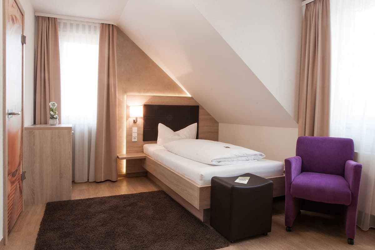 Un dormitorio con una cama, una mesita de noche, un aparador, un sillón morado y una pequeña mesa.