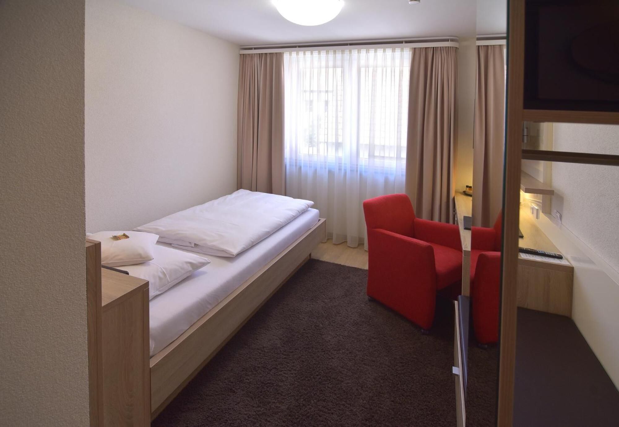 Una habitación pequeña y ordenada con una cama individual, un escritorio, una silla y un televisor.