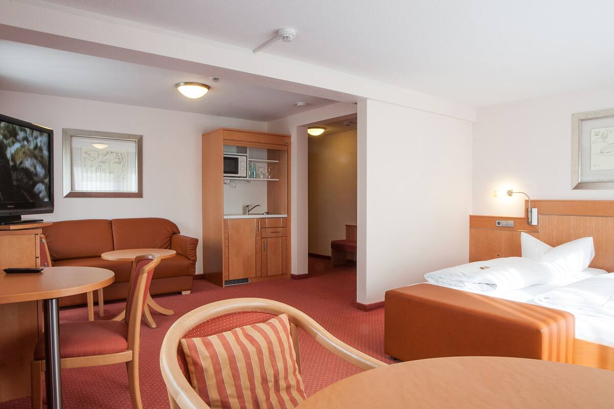 Una habitación de hotel con una cama, un sofá, una mesita, un televisor y un rincón americano.