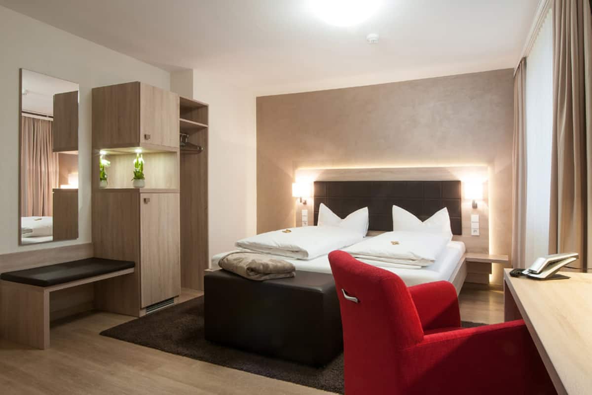 Habitación de hotel moderna con una cama grande, una silla roja, un escritorio, un banco y un armario.