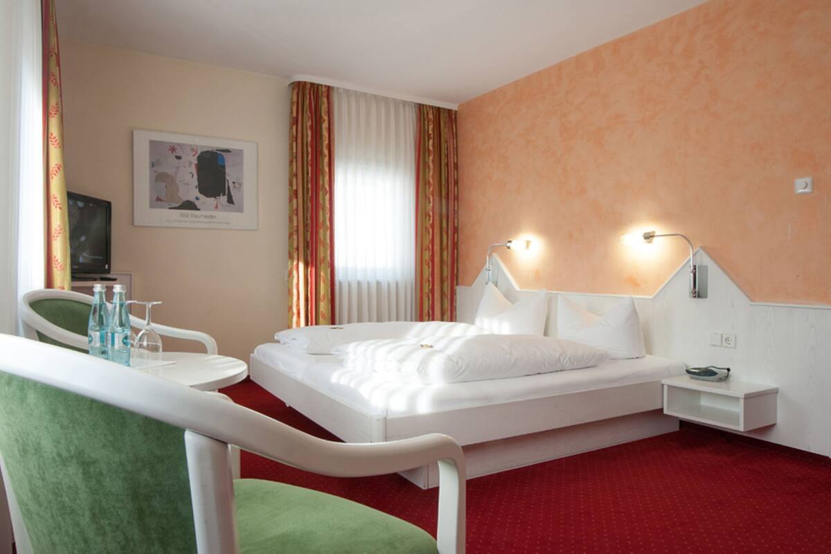 Una habitación de hotel con cama, mesita de noche, una silla, escritorio y televisión.