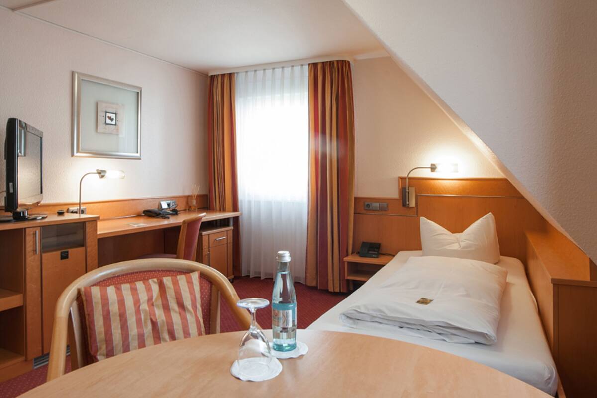 Una habitación de hotel con cama, escritorio, silla y una mesa con una botella y un vaso.