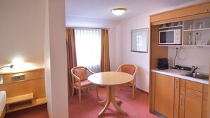 Quarto de hotel compacto com uma pequena mesa de jantar e duas cadeiras, micro-ondas e pia na cozinha compacta.