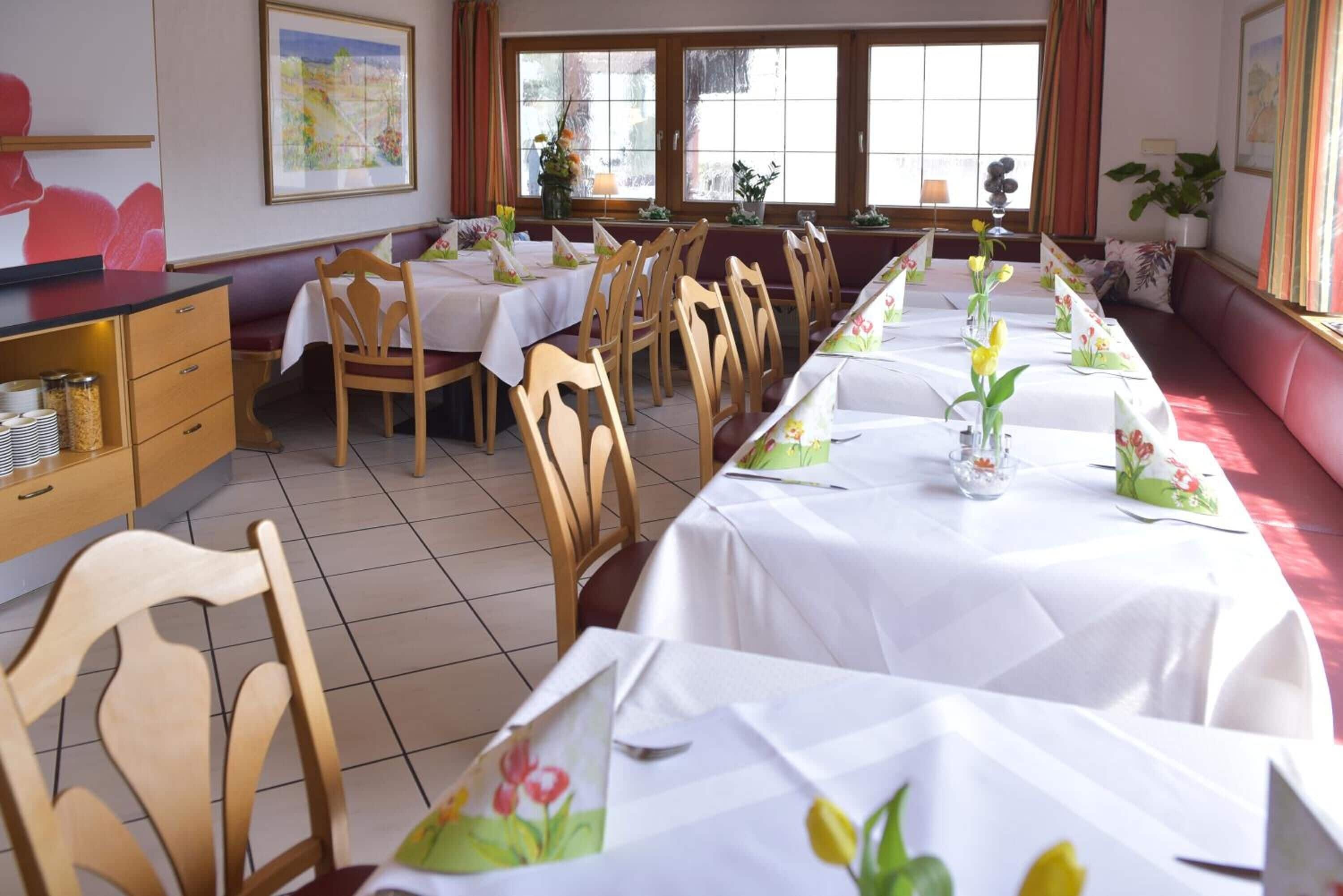 A dining area with multiple tables set for service, wooden chairs, and a long bench along the wall.